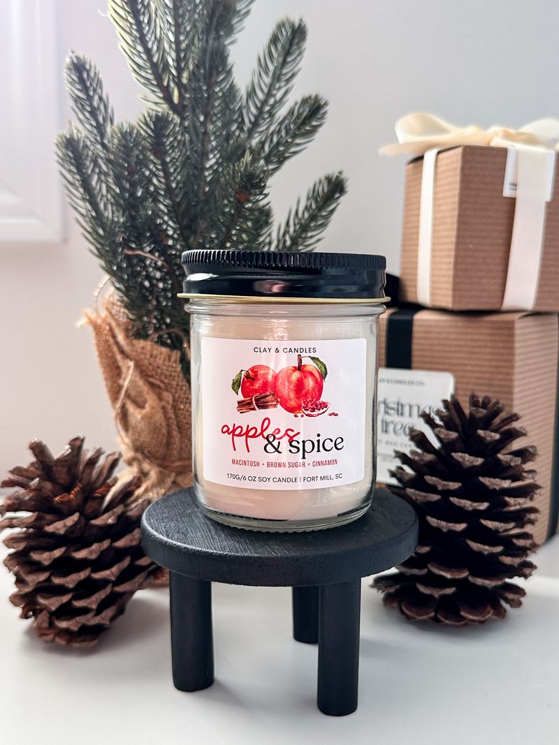 Apples and Spice candle on a black riser with pine cones and wrapped gifts