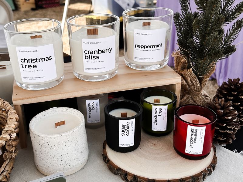 Holiday market table with Christmas Tree, Cranberry Bliss and Peppermint candles among pine cones